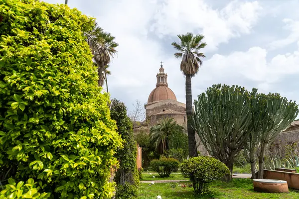Katanya 'daki yemyeşil manastır bahçesinde palmiye ağaçları, kaktüs bitkileri ve tarihi duvarların üzerinde yükselen San Nicola kubbesi parçalı bulutlu bir gökyüzünün altında..