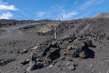 Gondels, engebeli kayalar, dik yamaçlar ve açık gökyüzünün altındaki sarı yosun parçalarıyla çevrili Etna Dağı 'ndaki karanlık volkanik araziyi geçer..