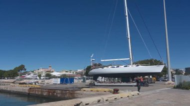 Cagliari - Sardinien - Italien - 03-10-2025: Vinç destekli liman işçileri ve teçhizat için beyaz bir yelkenli dikkatlice rıhtımın yakınında manevra yapılıyor.