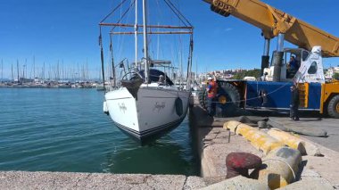 Cagliari - Sardinien - Italien - 03-10-2025: Peri masalı liman suyundan bir vinç tarafından kaldırıldı, rıhtım işçileri ve şehir silueti temiz gökyüzünün altında arka planda kaldı.