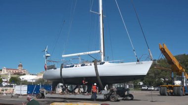 Cagliari - Sardinien - Italien - 03-10-2025: İşçiler arka planda görünen turna açık hava ve şehir manzarasıyla askıya alınmış beyaz bir yelkenli üzerinde son kontrolleri yapıyorlar.