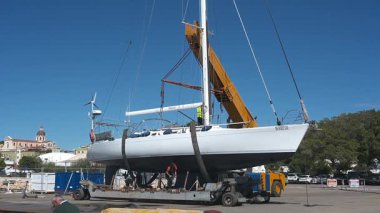 Cagliari - Sardinien - Italien - 03-10-2025: İşçiler arka planda görünen turna açık hava ve şehir manzarasıyla askıya alınmış beyaz bir yelkenli üzerinde son kontrolleri yapıyorlar.