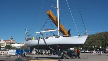 Cagliari - Sardinien - Italien - 03-10-2025: İşçiler arka planda görünen turna açık hava ve şehir manzarasıyla askıya alınmış beyaz bir yelkenli üzerinde son kontrolleri yapıyorlar.