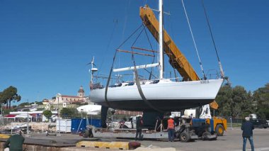 Cagliari - Sardinien - Italien - 03-10-2025: Alttaki römork kaldırılırken beyaz bir yelkenli vinç tarafından kaldırılıyor - işçiler ve şehir arkaplanı açıkça görülüyor.