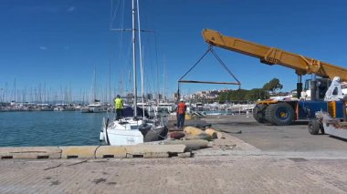 Cagliari - Sardinien - Italien - 03-10-2025: Limandaki işçiler bir yelkenliyi kaldırmak için seyyar bir vinç yerleştirilirken, diğer gemiler arka planda kenetleniyor.