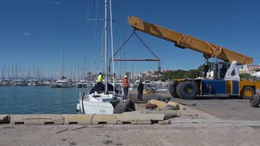 Cagliari - Sardinien - Italien - 03-10-2025: Limandaki işçiler bir yelkenliyi kaldırmak için seyyar bir vinç yerleştirilirken, diğer gemiler arka planda kenetleniyor.