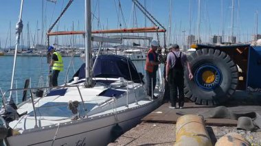 Cagliari - Sardinien - Italien - 03-10-2025: Birkaç işçi mavi gökyüzünün altında liman kenarında vinç kaldırma işlemi hazırlarken demirli bir yata zincir ve teçhizat taşıdılar.