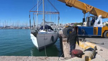 Cagliari - Sardinien - Italien - 03-10-2025: Peri masalı liman suyundan bir vinç tarafından kaldırıldı, rıhtım işçileri ve şehir silueti temiz gökyüzünün altında arka planda kaldı.