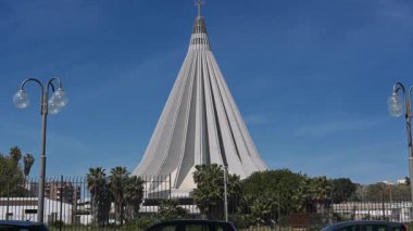 Syrakus, Sizilien - İtalya - 04-09-2025: Syracuse 'deki Santuario Madonna delle Lacrime, palmiye ağaçları ve sokak lambalarıyla çerçevelenmiş kendine özgü konik şekliyle dimdik ayakta duruyor.