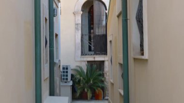 Syrakus, Sizilien - İtalya - 04-09-2025: Dar bir geçitten geçen dikey bir tava, bej konut binaları arasındaki eski balkonları, pencereleri, boruları ve klimaları ortaya çıkarıyor.