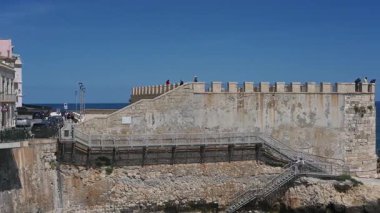 Syrakus, Sizilien - İtalya - 04-09-2025: Forte Vigliena üzerinde şehirden denize geniş bir pan, insanları platformda, basamaklarda ve kayalıklarda berrak gökyüzü ve parlak mavi su ile gösteriyor.
