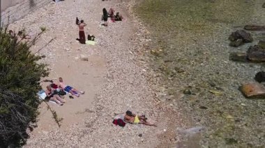 Syrakus, Sizilien - İtalya - 04-09-2025: İnsanların tarihi binaların yakınında güneşlendiği ve taş duvar boyunca sığ ve berrak suların bulunduğu küçük bir şehir plajı.
