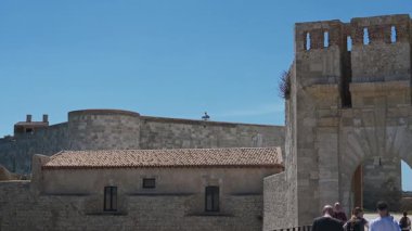 Syrakus, Sizilien - İtalya - 04-09-2025: Castello Maniace 'ın dış tarafındaki video panosu Syracuse, Sicilya' da güneşli bir gökyüzünün altında taş duvarlar, kapı kulesi, insanlar ve deniz ufkunu gösteriyor..