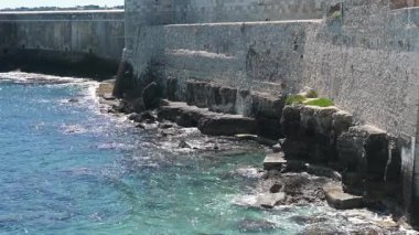 Syrakus, Sizilien - İtalya - 04-09-2025: Dalgalar, açık denizin antik taş duvarlar boyunca güneş ışığını yansıttığı Siraküza 'daki Castello Maniace' in altındaki kayalık kıyı şeridine vurdu.