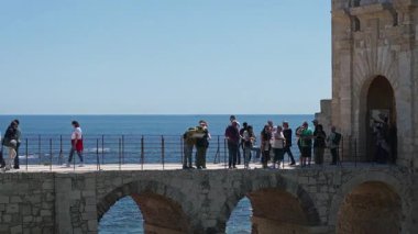 Syrakus, Sizilien - İtalya - 04-09-2025: Turistler, güneşli bir günde denize bakan büyük tarihi kapısından Castello Maniace 'e girmek için kemerli taş köprüden geçiyorlar.
