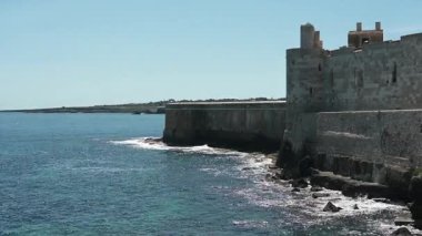 Syrakus, Sizilien - İtalya - 04-09-2025: Castello Maniace 'in sağlam taş duvarları denize bitişik, dalgalar yavaşça aşağıdaki kayalık kıyı şeridine çarpıyor.