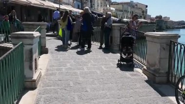 Syrakus, Sizilien - İtalya - 04-09-2025: İnsanlar Siraküza 'daki restoranların yanında, bebek arabaları, tenteleri ve açık havada güneş ışığında oturarak taş döşeli bir gezinti alanı boyunca yürüyorlar.