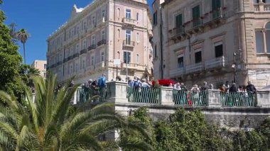 Syrakus, Sizilien - İtalya - 04-09-2025: Sicilya 'nın Syracuse kentinde açık mavi gökyüzü altında Fonte Aretusa köprüsü boyunca ayakta duran tarihi binalar ve turist grupları üzerinde durmak.