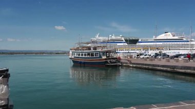 Syrakus, Sizilien - İtalya - 04-09-2025: Syrakus 'taki liman panoraması açık gün ortasında tekne, yolcu gemileri, tarihi binalar, park edilmiş arabalar, gezinti güvertesi ve mavi gökyüzünü gösteriyor.