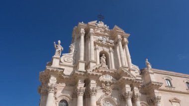 Syrakus, Sizilien - İtalya - 04-08-2025: Barok katedral cephesi ve halka açık meydanda gün ışığında mavi gökyüzü altında yürüyen, oturan veya toplanan insanlar.