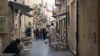 Syrakus, Sizilien - İtalya - 04-08-2025: Syracuslar 'da eski bir dar sokak insanlar, açık hava oturma yerleri, balkonlar ve taş cepheler ve dükkanlar boyunca dekoratif unsurlarla dolu.