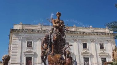 Syrakus, Sizilien - İtalya - 04-08-2025: Syracuse 'deki Diana Çeşmesi, açık mavi gökyüzü altında tarihi Palazzo Sicilya önünde mitolojik heykeller ve su jetleri barındırıyor..