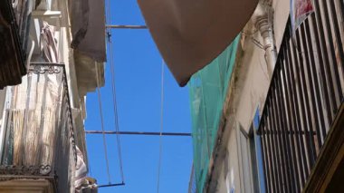 Syrakus, Sizilien - İtalya - 04-08-2025: Siraküza 'da dar bir sokaktaki binalar arasındaki kovayı kaldıran bir makara, çamaşırhaneleri, balkonları ve aşağıdaki insanları gösteriyor.