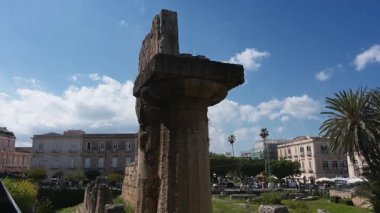 Syrakus, Sizilien - İtalya - 04-08-2025: Dağınık sütunlar, yeşillikler, pazar çadırları ve tarihi binalar ile antik Apollon tapınağının panoramik manzarası.