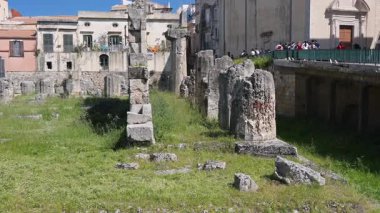 Syrakus, Sizilien - İtalya - 04-08-2025: Muazzam taş sütunları ve çimenli arazisi olan antik Apollon tapınağı kalıntıları, konut binaları ve bir kilise ile çevrili.