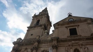 Ragusa 'daki ana katedralin görüntüsü. Süslü bir cephe, çan kulesi ve bulutlu bir gökyüzünün altındaki heykeller..