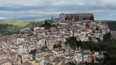 Ragusa, Sizilien - İtalya - 04-03-2025 Redaktionell: Arka planda büyük bir taş yapı ve yeşil kırsal alan bulunan Ragusa Ibla 'nın bir tepedeki tarihi binalarını sıkıca kaplayın.
