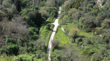 Ragusa 'nın kuzeyindeki vadi, teraslı yamaçlar, yoğun bitki örtüsü, toprak yol ve yeşil araziyi kaplayan eski bir viyadük manzarası..