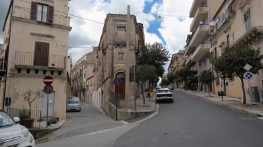 Ragusa, Sizilien - İtalya - 04-03-2025 Redaktionell: Ragusa 'da sol ve sağ tarafında arabalar, ağaçlar ve modern balkonların yer aldığı dar ve eski caddeleri gösteren bölünmüş yol manzarası.
