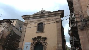 Ragusa, Sizilien - İtalya - 04-03-2025 Redaktionell: Ragusa 'da düz bir cephe, barok tarzı giriş kemeri, tek pencere, çatı haçı ve çevre kentsel binalara sahip küçük bir kilise manzarası.