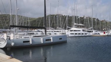 Portisco - Sardinien - Italien - 02-23-2025: Geniş bir liman manzarası demirlemiş yatlar ve yelkenlileri, durgun mavi su, marina tesisleri ve arkadaki yeşil tepeleri gösteriyor.