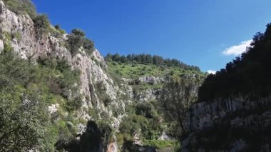 Güneşli kayalık kanyon, yeşil yamaçlar ve Pantalica 'da dar bir patika, kayalıklar, bitki örtüsü ve dağınık kayaların doğal zemini şekillendirdiği yer..