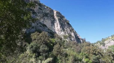 Pantalica, Sizilien - İtalya - 04-11-2025: Açık mavi gökyüzü altındaki kireçtaşı uçurumları ve gür bitki örtüsü boyunca esen geniş yol Pantalicas arazisi ve doğal güzelliği gösteriyor.