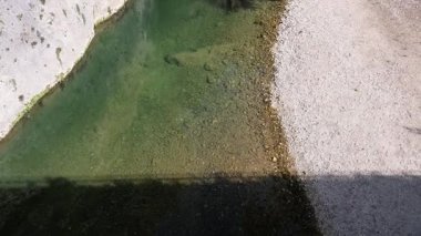 Ağaçlar, uçurumlar ve güçlü bahar ışığı altındaki yansımalarla çevrili dikey kaya duvarları ve çakıllı kıyılar arasında berrak bir dere akar..