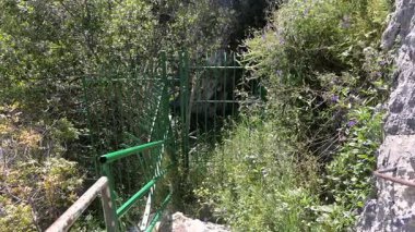 Pantalica, Sizilien - İtalya - 04-11-2025: Pantalica vadisinde kayalık kayalıklar, yeşil bitki örtüsü ve dik bir doğal ortamda çitli bir yol gösteren geniş bir manzara.