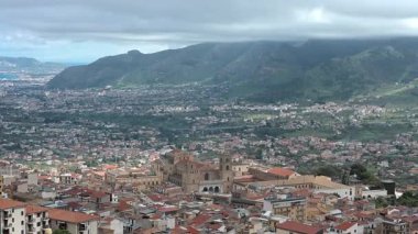 Monreale - Sizilien - Italien - 03-18-2025: Monreale üzerinde panoramik soldan sağa manzara katedrali, çatıları, yuvarlanan tepeleri ve Sicilya 'daki dağınık bulutların altındaki uzak Palermo sahillerini gösteriyor.