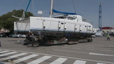 Cagliari - Sardinien - Italien - 03-14-2025: Liman işçisi bakım işlemleri için bir katamaranı limanın karşısındaki kuru rıhtıma taşımak için bir nakliye römorku işletiyor.