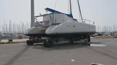 Cagliari - Sardinien - Italien - 03-14-2025: Bir katamaran nakliye karavanında güvence altına alındı ve sudan çıkarıldı, park halindeki araçlar ve marina altyapısını geçti.