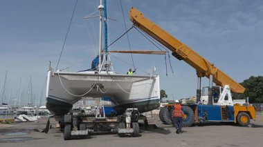Cagliari - Sardinien - Italien - 03-14-2025: Katamaranı nakliye platformuna yerleştirdikten sonra, vinç geri çekiliyor ve mürettebat kaldırma kayışları ve aletleri topluyor.