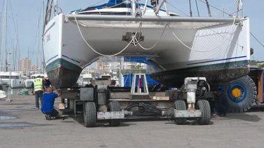 Cagliari - Sardinien - Italien - 03-14-2025: İşçiler taşımacılık aracındaki katamaranı daha ileri gitmeden önce dengeli ve güvenli bir konum sağlayarak denetleyip emniyete alıyorlar.