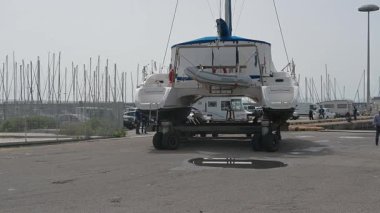 Cagliari - Sardinien - Italien - 03-14-2025: Bir katamaran nakliye karavanında güvence altına alındı ve sudan çıkarıldı, park halindeki araçlar ve marina altyapısını geçti.