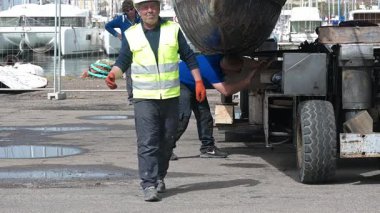 Cagliari - Sardinien - Italien - 03-14-2025: Sudan kaldırıldıktan sonra bir katamaranın omurgası altında dinlenen üç işçi tahta destekleri.