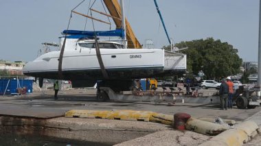 Cagliari - Sardinien - Italien - 03-14-2025: İşçiler tekneyi hizaya sokarken bir katamaran vinç tarafından aşağıda bir nakliye platformu olarak askıya alındı.