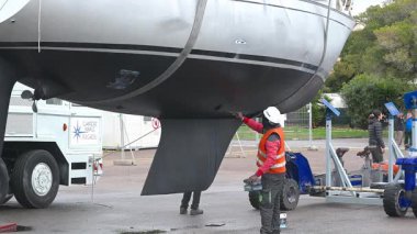 Cagliari - Sardinien - Italien - 03-12-2025: İşçiler daha önce kuru rıhtım sırasında destek çerçevesiyle temas halinde olan yelkenli teknesinin gövdesini kazıyor, kumlanıyor ve yeniden boyuyorlar.