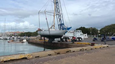 Cagliari - Sardinien - Italien - 03-12-2025: Bir vinç mürettebatı yelkenliyi suya indirirken, işçiler fırlatma sürecinin son safhasında gemiyi halatlarla dengede tutuyorlar.
