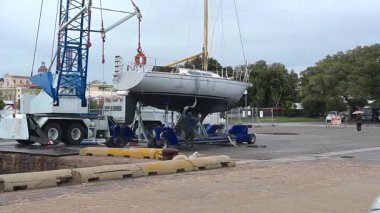 Cagliari - Sardinien - Italien - 03-12-2025: İşçiler, Cagliari 'de bulutlu gökyüzünün altında bir limanda vinç kullanarak bir yelkenlinin gövdesine ağır yük kaldırma kolları takıyorlar.